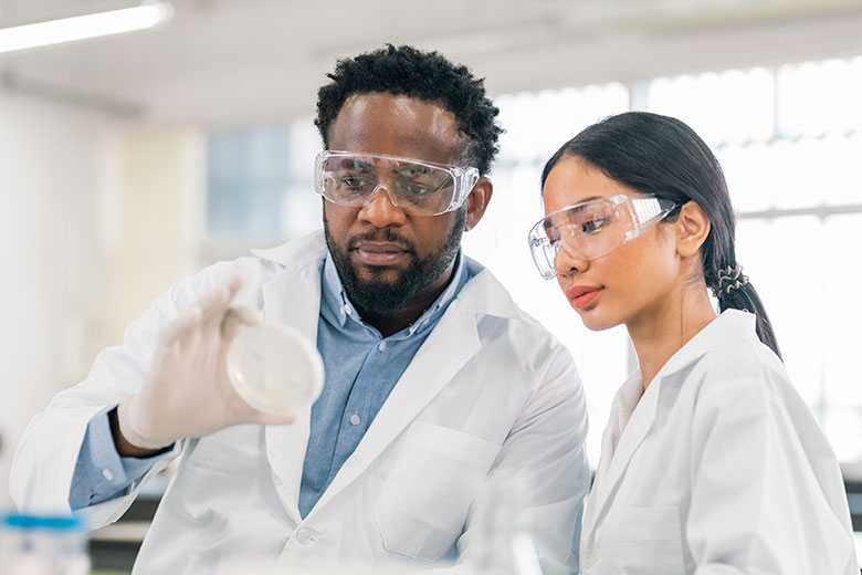Two researchers closely examine a petri dish