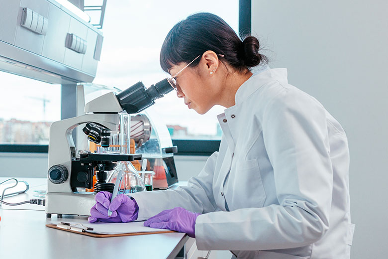 Researcher takes notes as she looks into a microscope